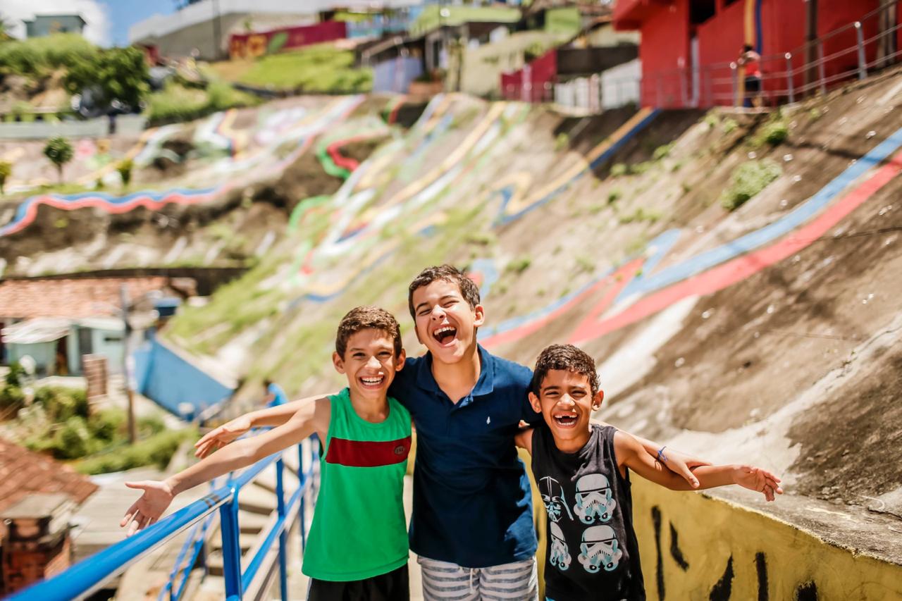 Três meninos posam para a foto, no bairro Vasco da Gama. Eles riem.