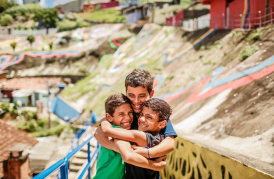 Três meninos se abraçam, sorridentes, no bairro Vasco da Gama