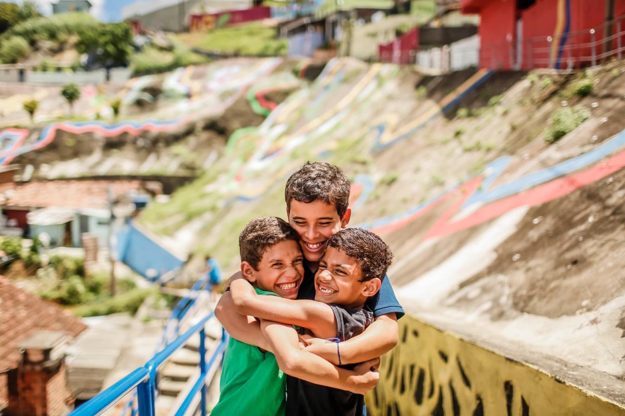 Três meninos se abraçam, sorridentes, no bairro Vasco da Gama